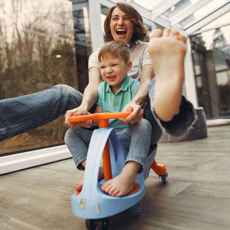 A mother and child racing on a push scooter with wild smiles on their faces.